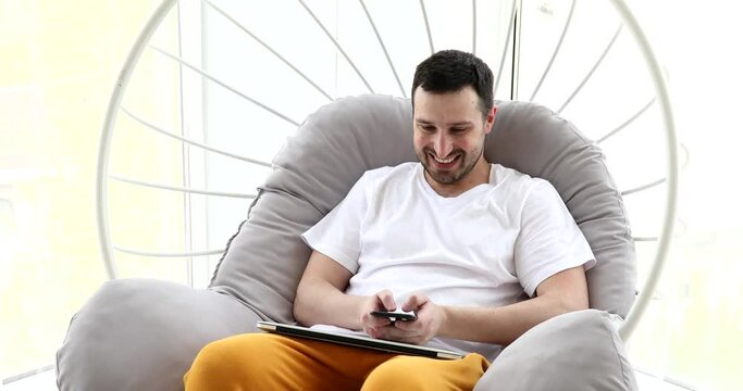 Happy Young Man Uses Smartphone while Sitting on a Sofa at Home.
