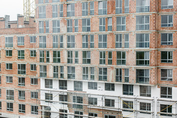 Fototapeta premium Unfinished building with brick walls and many windows. Building construction site. Development in the city, skyscraper build. Investing in real estate