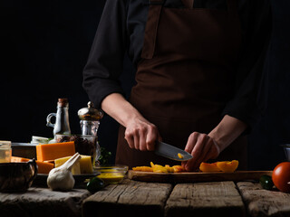 Stuffed goose. The chef is cutting oranges on a cutting board. There are also ingredients in the frame: garlic, cheese, sauce, spices. A festive dish. Bright paints, dark background.
