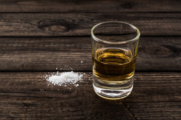 Glass of tequila with salt on an old wooden table. Close up view