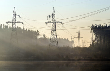 Power line in the cleared area of the forest. Steel electro masts with wires by the lake.