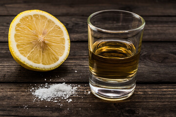 Glass of tequila and half a lemon with salt on an old wooden table. Close up view