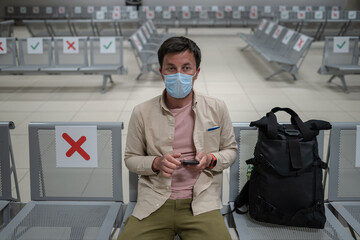 Fototapeta na wymiar Man wearing protective mask upset by cancellation flight, writes message to his family, sitting in empty terminal at airport of Cyprus, Paphos city, due to coronavirus pandemic of Covid 19 outbreak