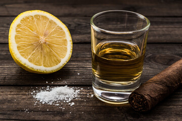 Glass of tequila and half a lemon with salt and cuban cigar on an old wooden table. Close up view