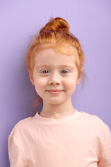 cute smiling caucasian child girl with red hair and big blue eyes isolated over purple background....