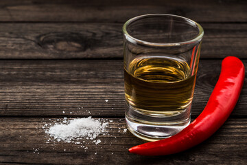 Glass of tequila with cayenne pepper and salt on an old wooden table. Close up view