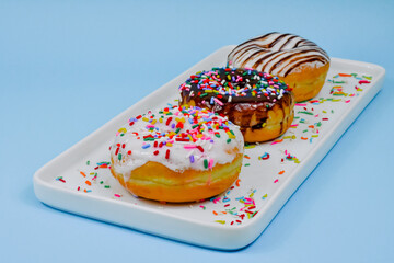 Deliciosas donas rellenas con chispas de colores y diferentes sabores sobre fondo celeste