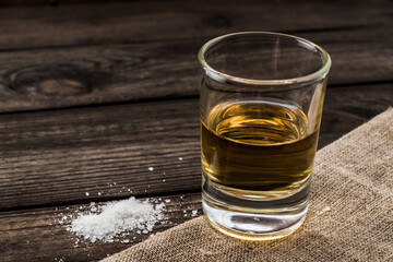 Glass of tequila and piece of cloth with salt on an old wooden table. Close up view