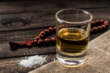 Glass of tequila and piece of cloth with salt and rosary on an old wooden table. Close up view