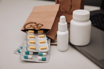 Pills and spray containers and buff paper bags near laptop close-up. Online pharmacy concept