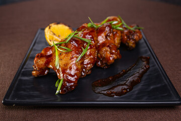 baked chicken wings with sauce and herbs on a black plate