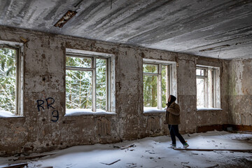 The young man with pink blonde hair in fluffy coat and black hoodie standing near the window without glass in old ruin abandoned urban building