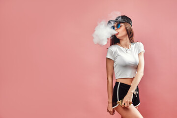 Seductive glamour young woman standing and vaping on pink background