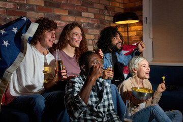 International group of student friends hanging out at home huddled on couch together excitedly watching event on TV drinking beer, anticipating winning goal. american football, basketball, tennis