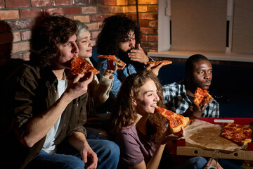 happy friends eating pizza and watching movie or tv series at home, american students enjoy spare...