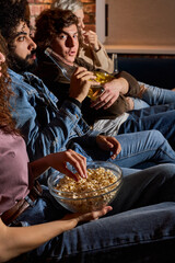 Close-up photo of friends watching comedy eating popcorn snacks in bowl and drinking beer, side view on young people watching interesting movie at home