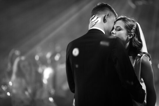 Portrait of newlyweds first wedding dance. Just married couple dancing in darkness. Groom holds bride's hand dancing with her in the middle of restaurant. Happy bride and groom and their first dance. - Powered by Adobe