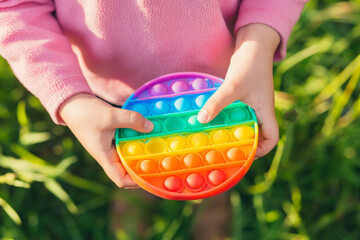Colorful antistress sensory toy fidget push pop it in kid's hands - obrazy, fototapety, plakaty
