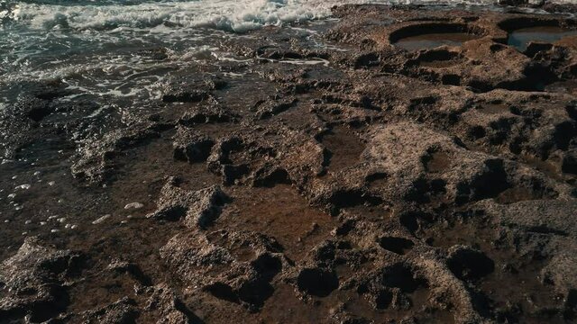Waves washing rocky coast with salt pools. Bugibba Bay malta ascending tilt down shot. High quality 4k footage