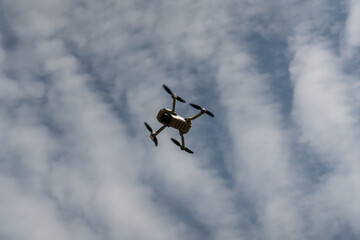 Silhouette of a drone on a background of blue sky and clouds. You are being followed. You are being filmed.