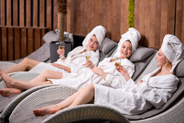 Relaxed ladies enjoy drinking champagne at spa. Three beautiful caucasian women wearing bathrobes having cool resting, holidays in wellness center