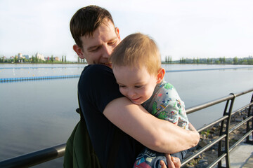 Fototapeta na wymiar Smiling and happy father hugs the child. Cheerful family by the river