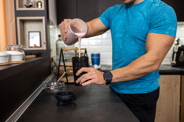 Fototapeta na wymiar Close up of a muscular man making a shake in the kitchen of his flat