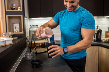 Young man pouring a tasty berry shake into his drinking cup in the kitchen, delicious healthy treats