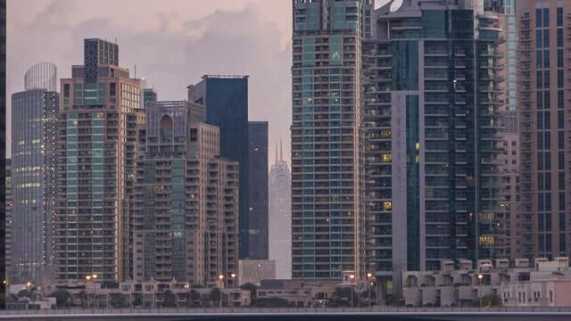 Dubai Marina canal, waterfront with modern towers and yachts reflected in water from bridge in Dubai night to day transition timelapse, United Arab Emirates. Skyscrapers around before sunrise