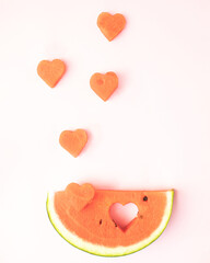 Obraz na płótnie Canvas A refreshing watermelon and a flying heart on a light pink background. Minimal summer flat lay