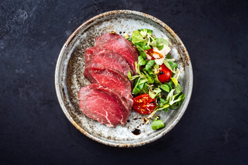 Modern style gourmet raw Japanese tataki beef filet with lettuce and tomatoes as top view on a...