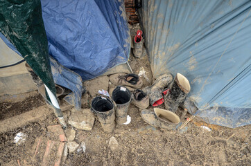 Shoes of migrants in front of tent in camp. Dirty shoes of refugees in an unconditional camp.