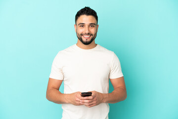 Young arab man isolated on blue background sending a message with the mobile