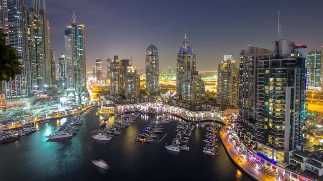 Aerial top view day to night transition timelapse of Dubai Marina promenade and canal with floating yachts and boats after sunset in Dubai, UAE. Modern towers and traffic on the road from above