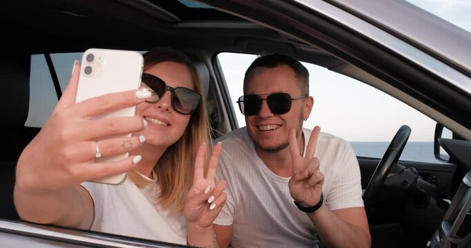 Young Man and Woman Having Fun and Taking Selfie on Smartphone in Car with Sea View from Window, Travel and Roadtrip in Summertime