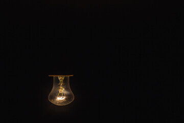 The old incandescent lamp with a tungsten filament. Light bulb close-up isolated black background.