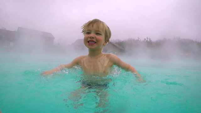 Geothermal spa resort. Cute little child boy having fun in hot spring pool outdoors in the mountains. Bathing in hot water, offseason travel attraction.