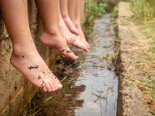 Bare and dirty feet of children sitting by the river on a summer afternoon. Concept of freedom in the game, happy childhood
