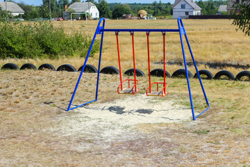 Fototapeta premium Defocus swing on playground on countryside area background. Bright blue and red swing. Family summer game. Out of focus