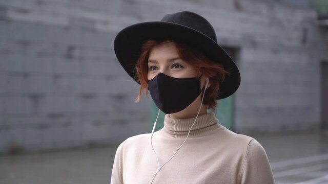 Stylish woman wearing protective face mask listening music walking on the street. Slow motion. Health care concept 