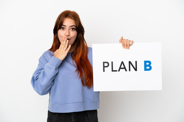 Young redhead woman isolated on white background holding a placard with the message PLAN B with surprised expression