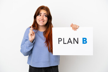 Young redhead woman isolated on white background holding a placard with the message PLAN B with fingers crossing