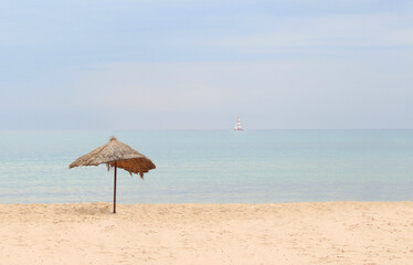 Straw beach umbrella on a tropical sandy beach on a background of blue sea on a sunny day. Idyllic travel and summer vacation concept. Beach umbrella with straw on the sand on a background of blue sea