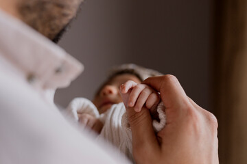 Close up of young father holding the hand of his newborn baby at home - Happy hispanic father...