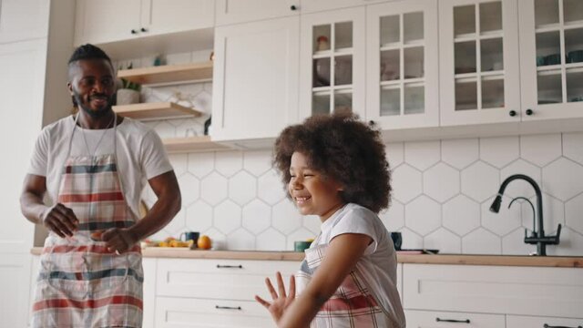 Happy time together. Positive little african american girl dancing at kitchen together with her daddy, slow motion