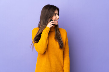 Teenager Brazilian girl over isolated purple background keeping a conversation with the mobile...