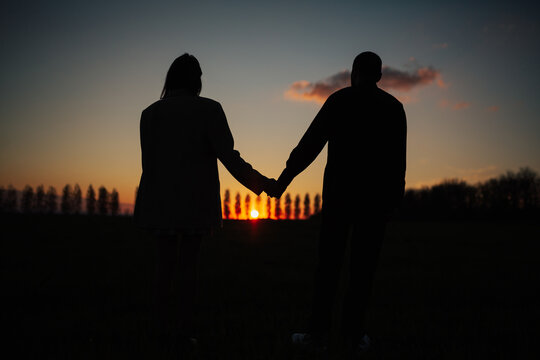 A dark silhouette of romantic couple holding hands and watching a beautiful sunset. Romantic moment.