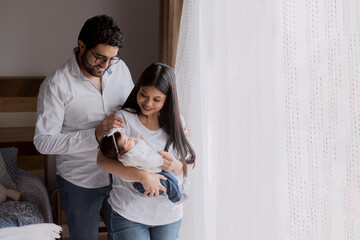 Young hispanic parents holding their newborn baby at home- parents in love taking home their newborn baby- small latin family - obrazy, fototapety, plakaty