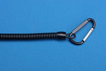 one metal carabiner latch on a black spiral wire lies on a blue table