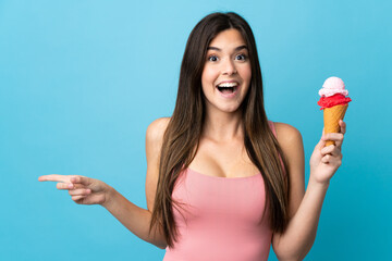 Teenager Brazilian girl holding a cornet ice cream over isolated blue background surprised and...